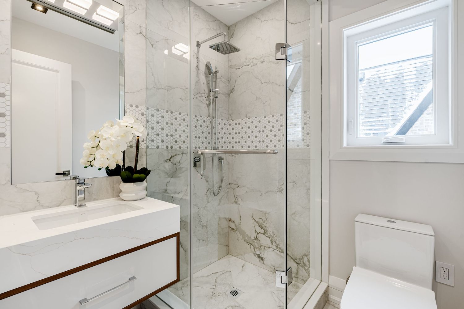 White marble bathroom with glass shower enclosure and contemporary fixtures.