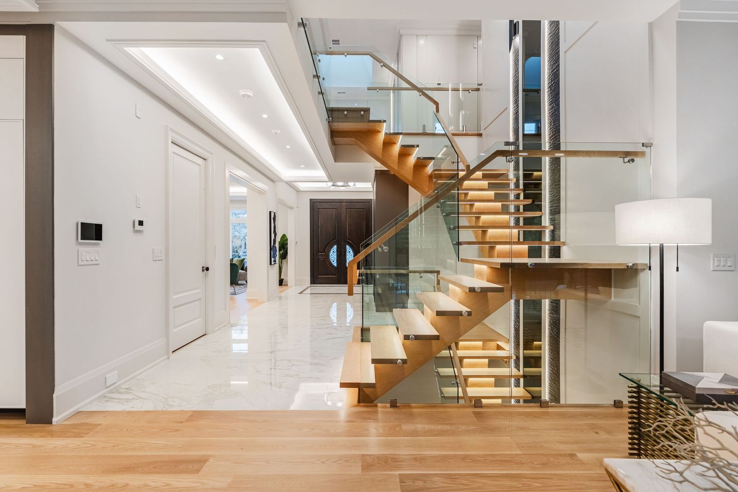 Contemporary staircase with glass railings, wooden treads, and bright hallway leading to upper level.
