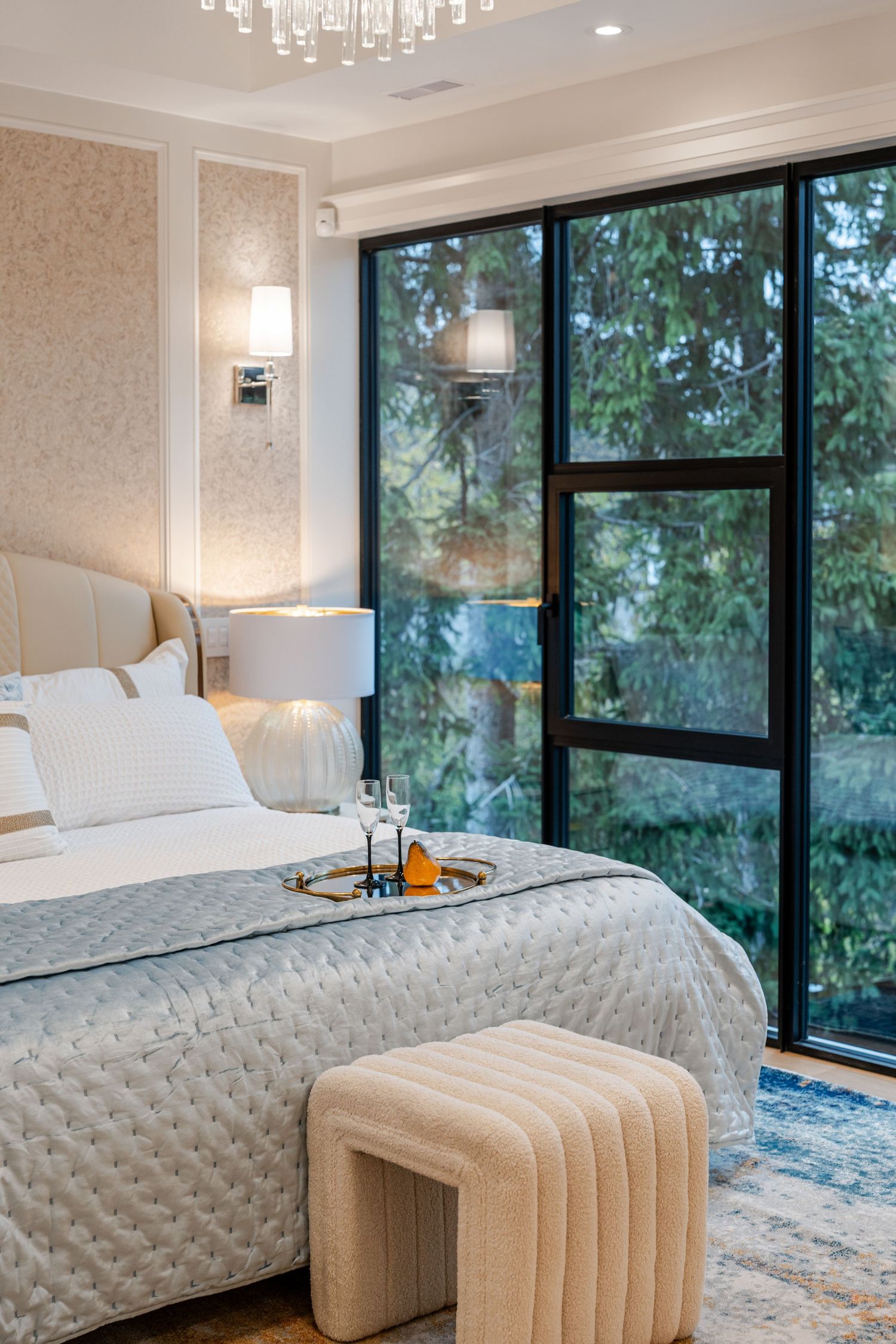 Luxurious bedroom with floor-to-ceiling windows, crystal chandelier, and textured bedding.