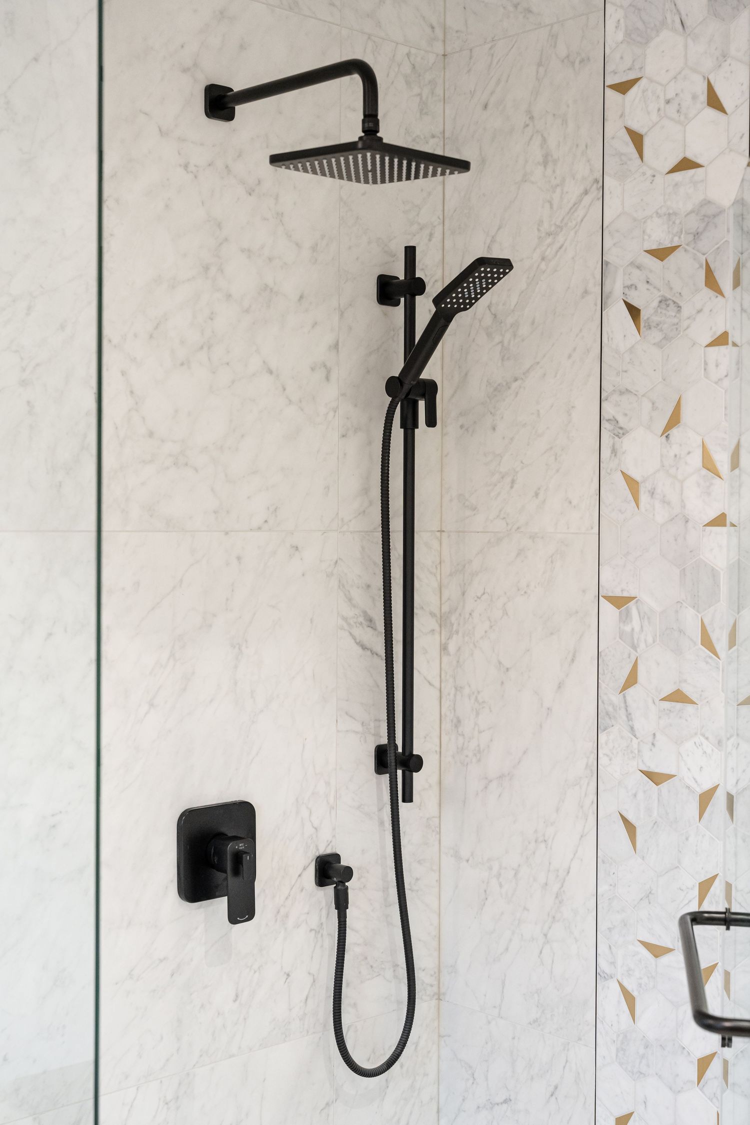 Modern black rainfall shower head and handheld shower system mounted on white marble bathroom wall.
