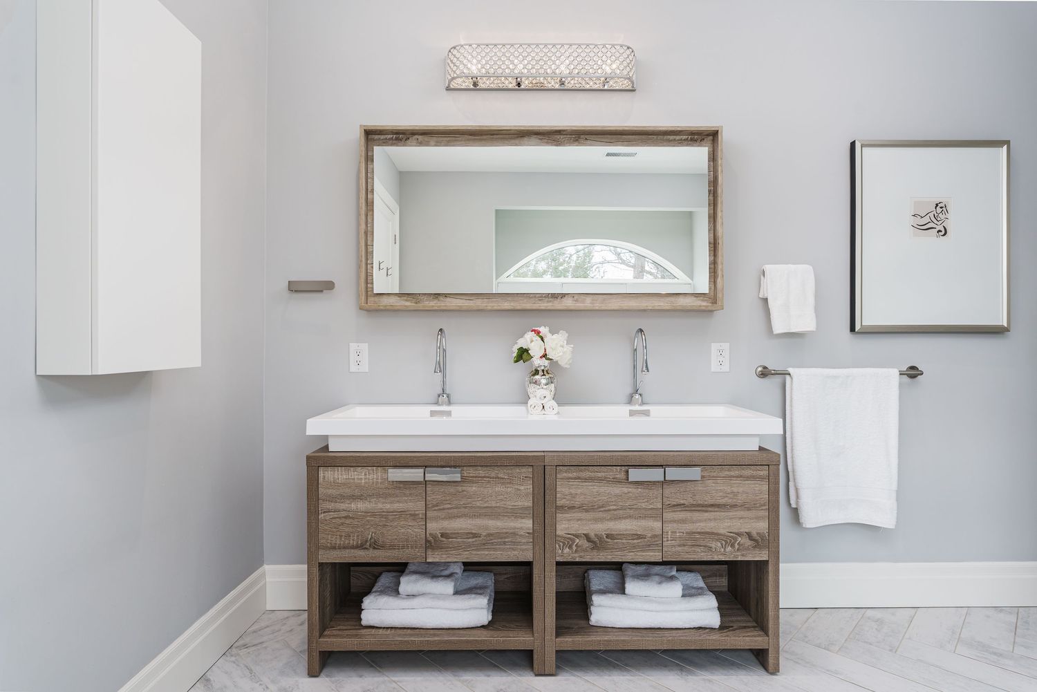 Modern bathroom vanity with wooden base cabinet, white countertop sink, framed mirror and light gray walls.