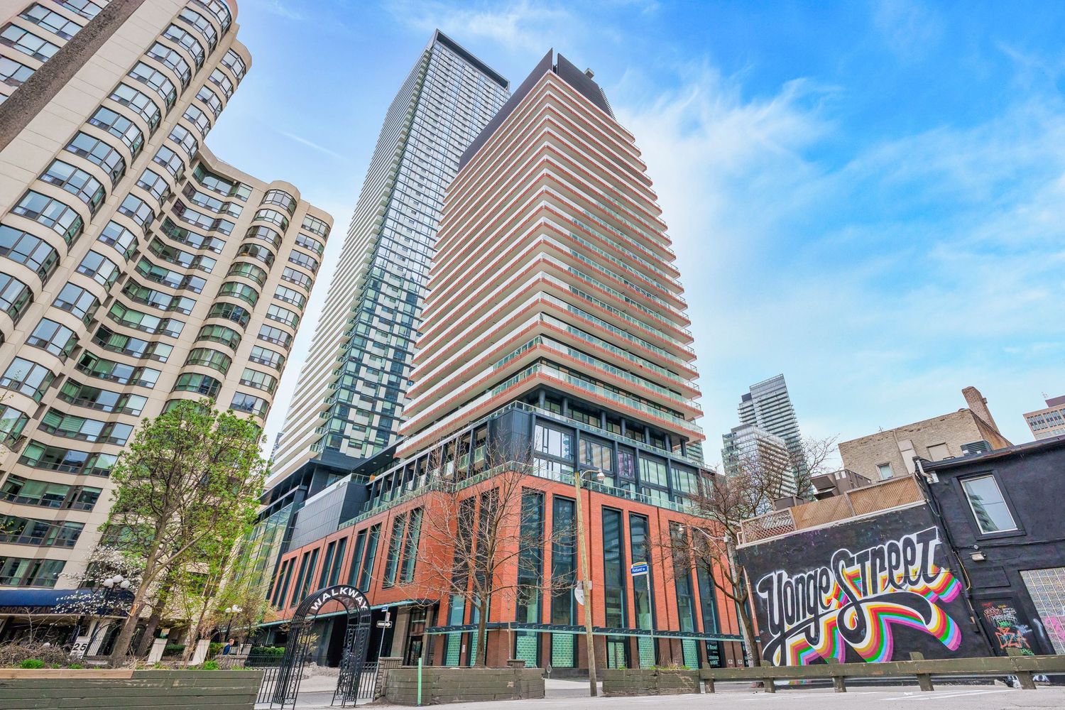 Modern residential condominium towers with glass balconies rise against a bright blue sky in an urban neighborhood in downtown toronto