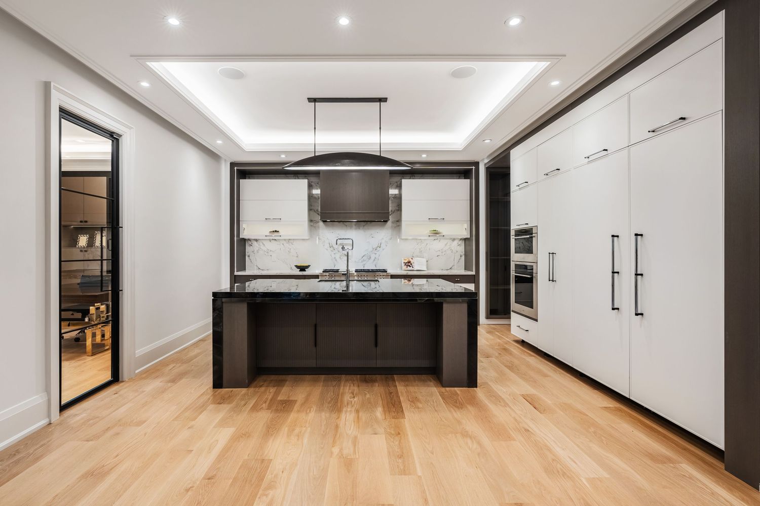 Contemporary white kitchen with minimalist design, recessed lighting, and wide plank hardwood flooring.