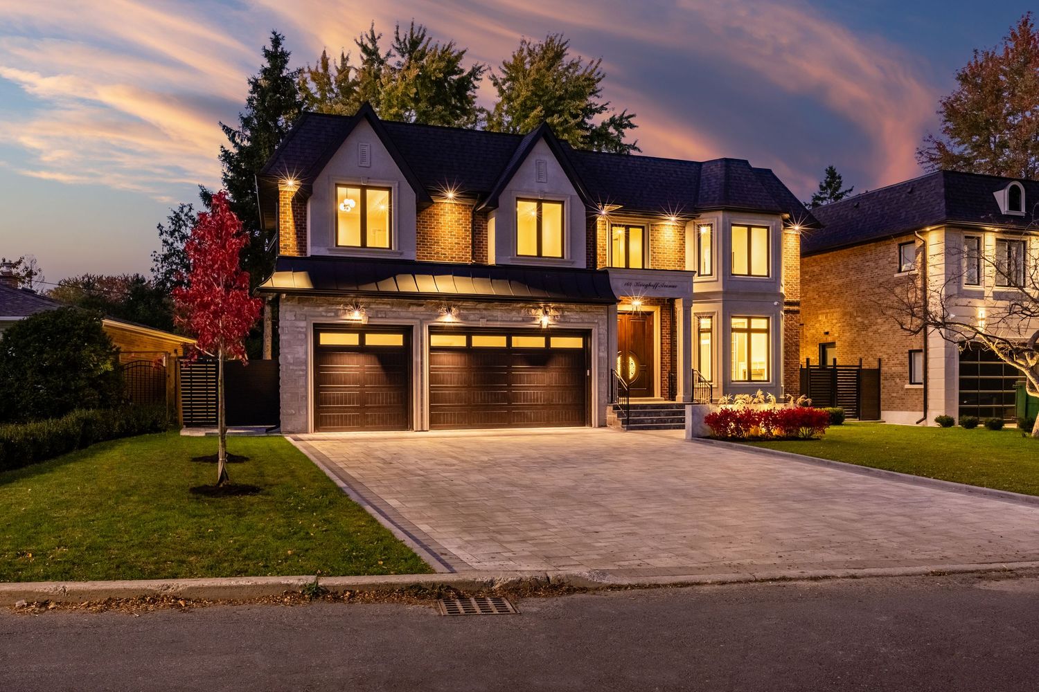 Modern residential house exterior with illuminated windows and red autumn tree at twilight.