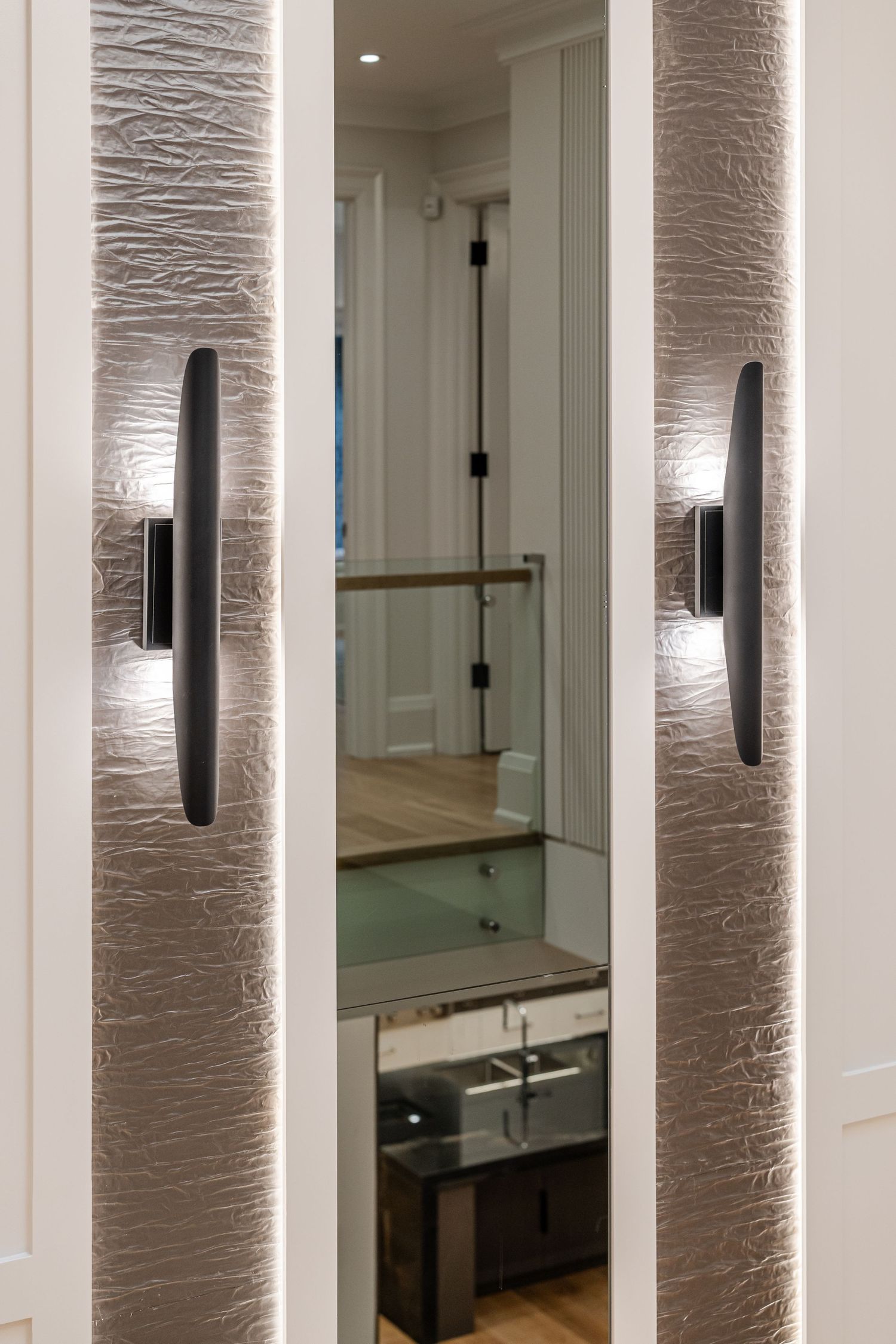 Textured wall panels with modern black sconces frame a mirrored closet door.