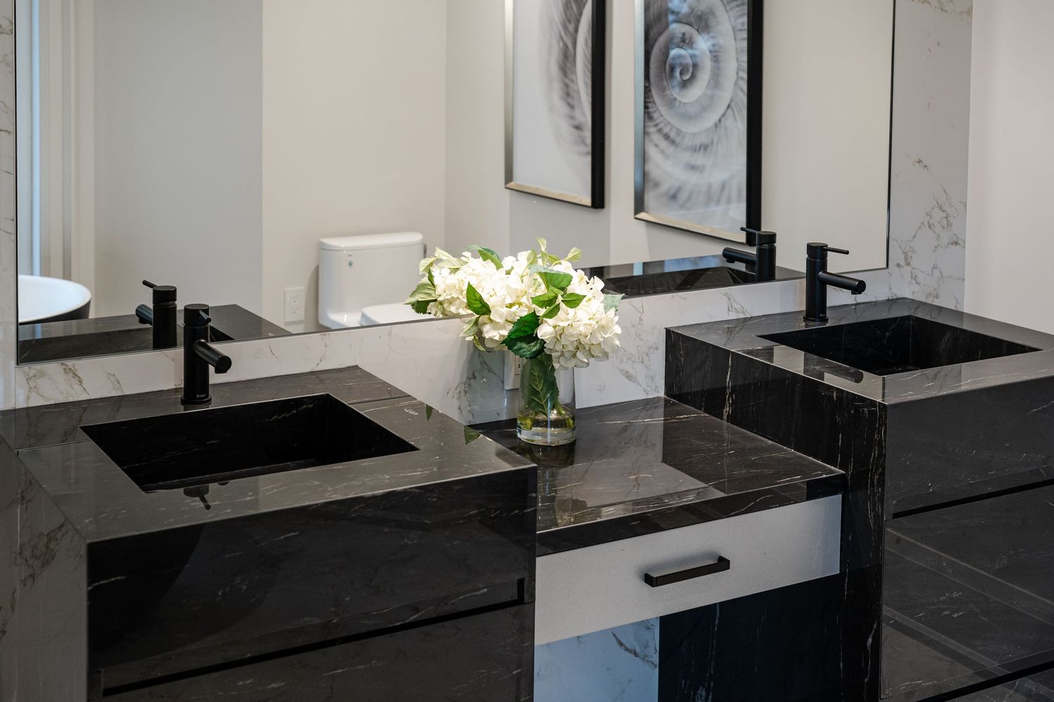 Elegant bathroom vanity with black vessel sinks, fresh flowers, and marble wall finishes.
