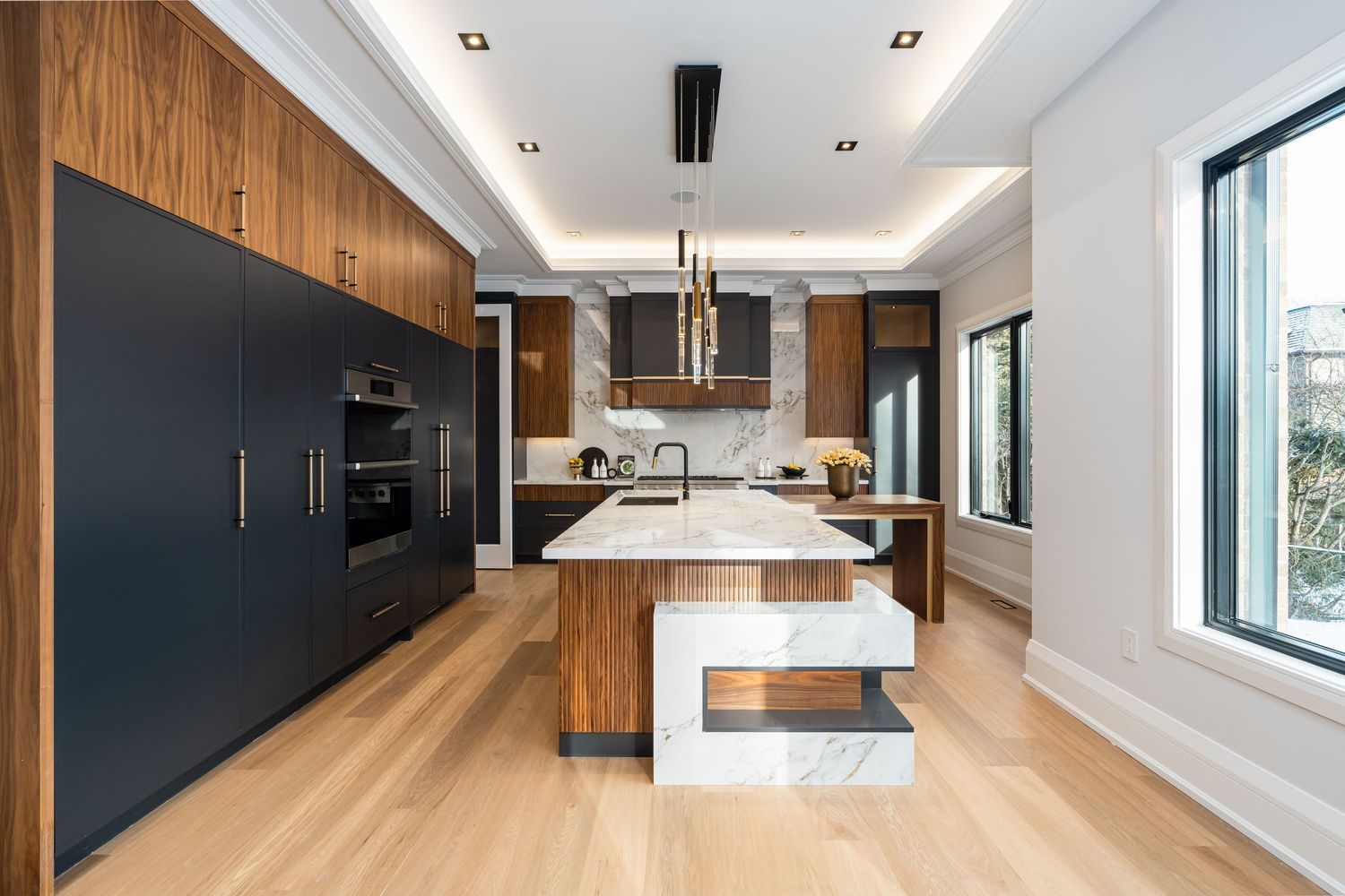 Contemporary kitchen design with black and wood cabinetry, white countertops, and light hardwood flooring.
