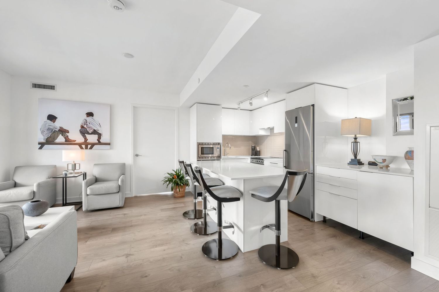 Modern open concept condo interior with light gray furniture, white kitchen and hardwood floors in minimalist style.