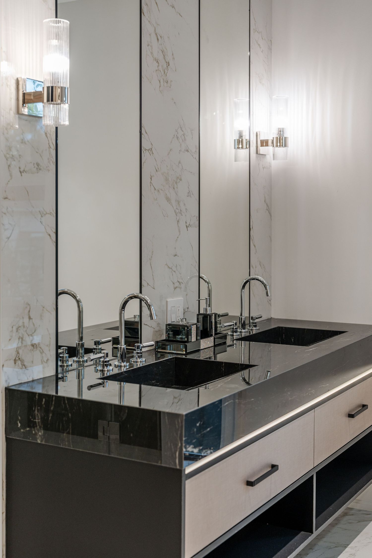 Modern bathroom vanity with multiple black sinks and chrome fixtures against marble walls.