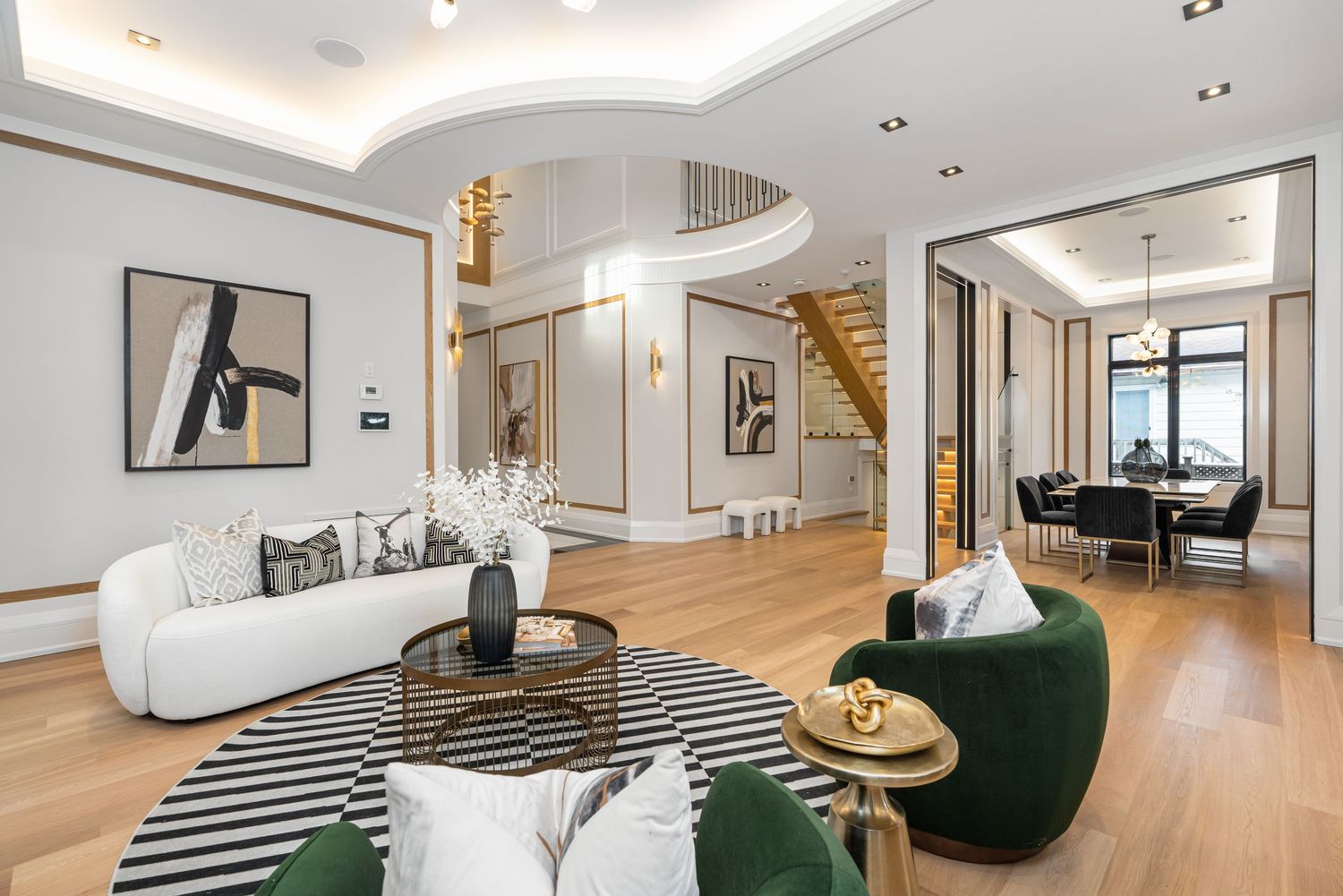 Open concept living space showcases minimalist decor with emerald accent chairs and striped cushions.
