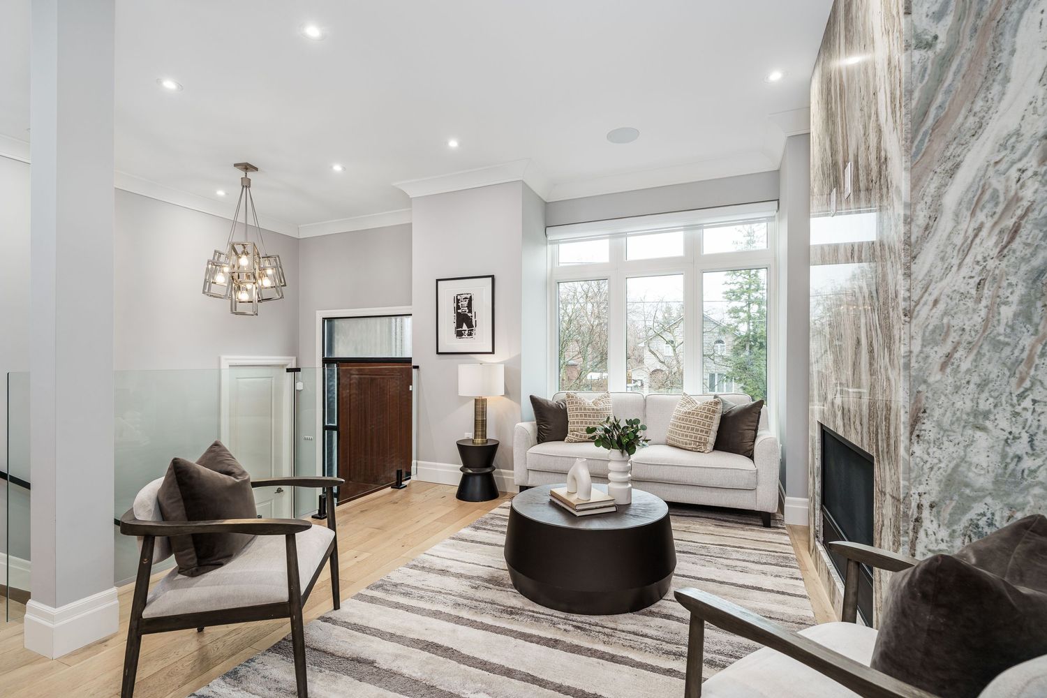 Modern living room with white walls, marble fireplace, circular coffee table and elegant chandelier in natural light.