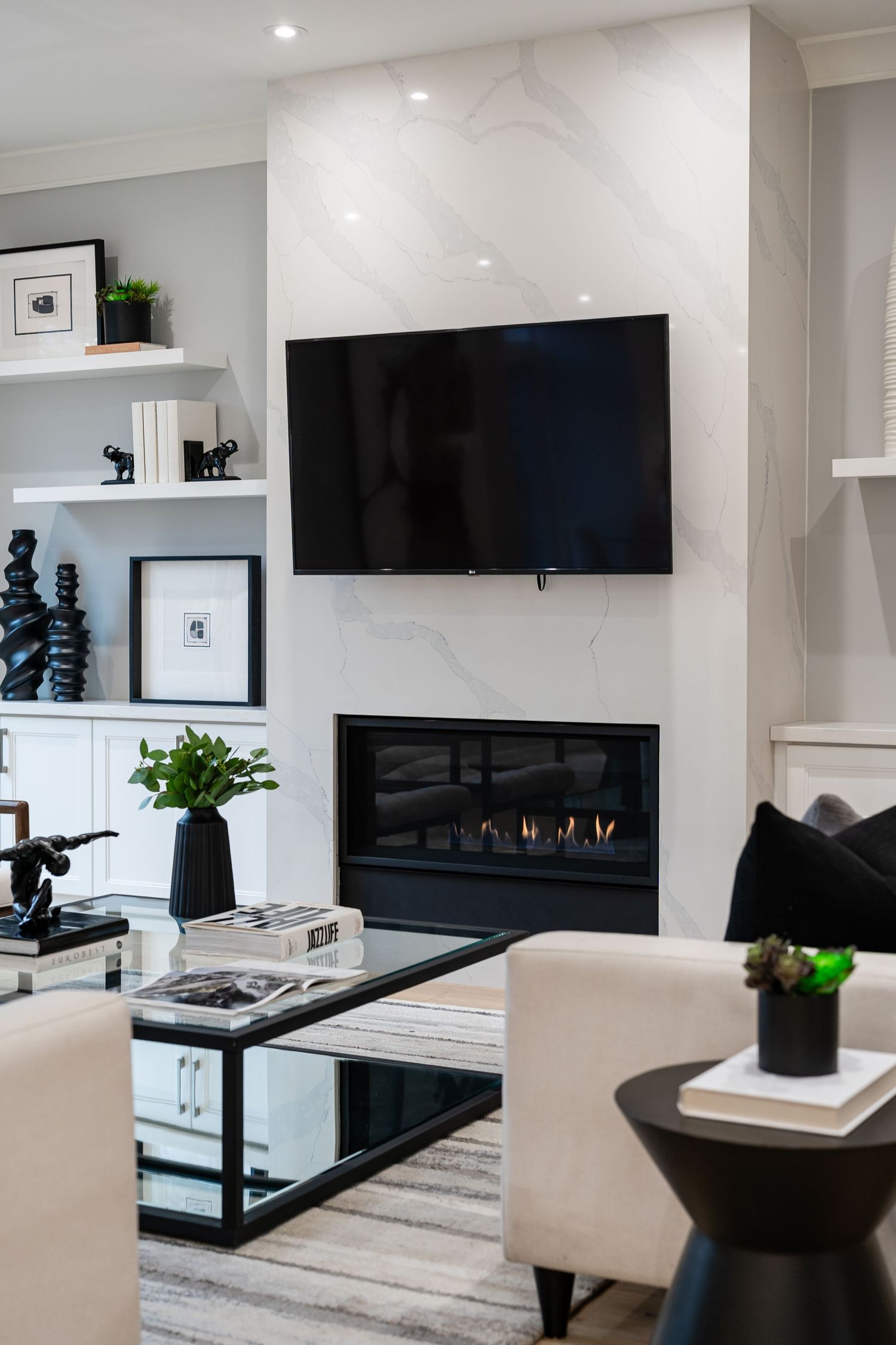 Modern living room features a mounted flat-screen TV above gas fireplace with white built-in shelving and black accents.
