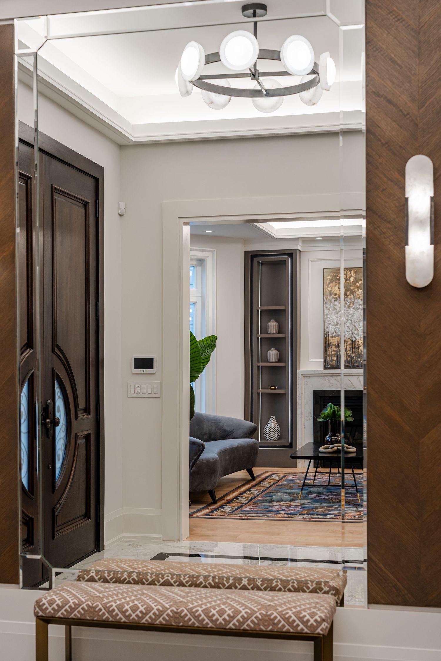 Elegant foyer with dark wood doors, crystal chandelier, and upholstered bench seating.