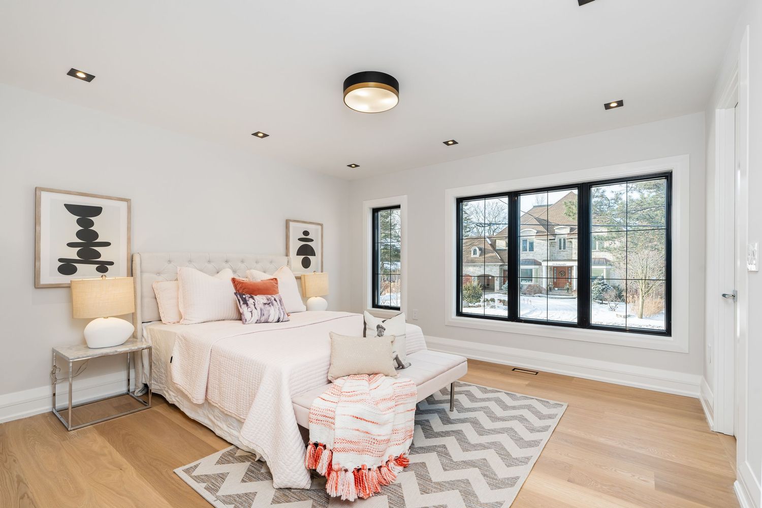 Bright modern bedroom with large windows, geometric rug, and neutral decor scheme.