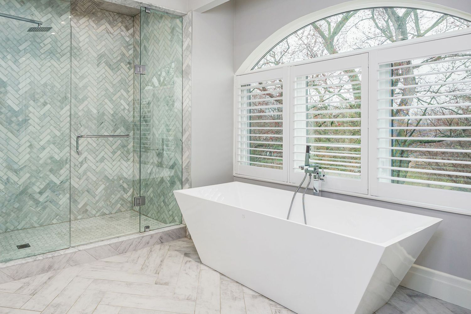 Modern luxury bathroom with freestanding white bathtub, glass shower enclosure, and mint herringbone tile wall design.