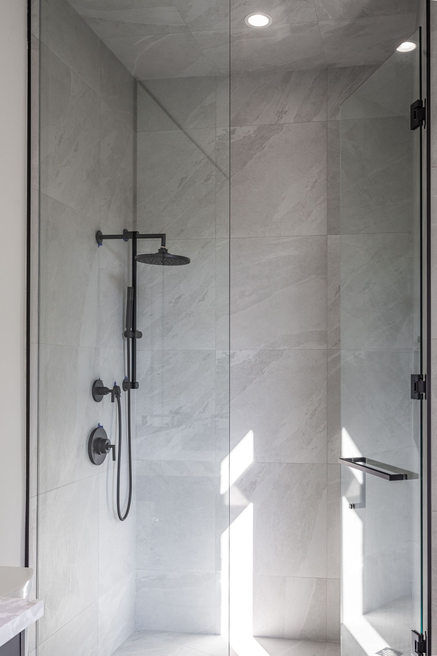 Luxurious walk-in shower with marble tile walls and matte black fixtures capturing natural sunlight.