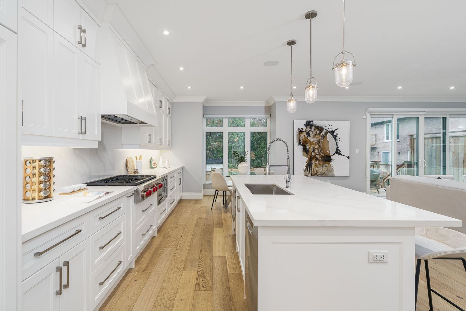 Modern white kitchen with hardwood floors features pendant lights, quartz countertops and custom cabinetry in open concept design.