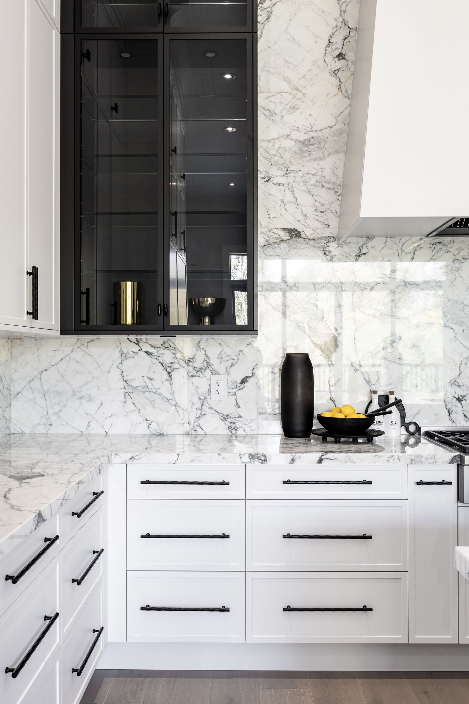 Elegant white kitchen with black glass cabinet doors and marble wall featuring modern hardware.