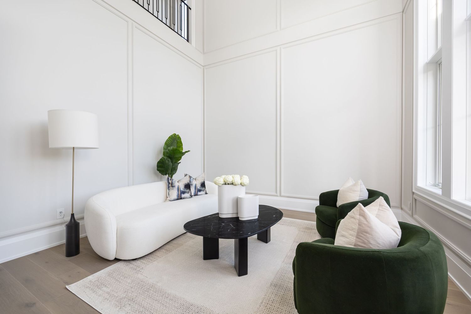 Modern sitting area with curved white sofa, black accent tables, and emerald green velvet chair.