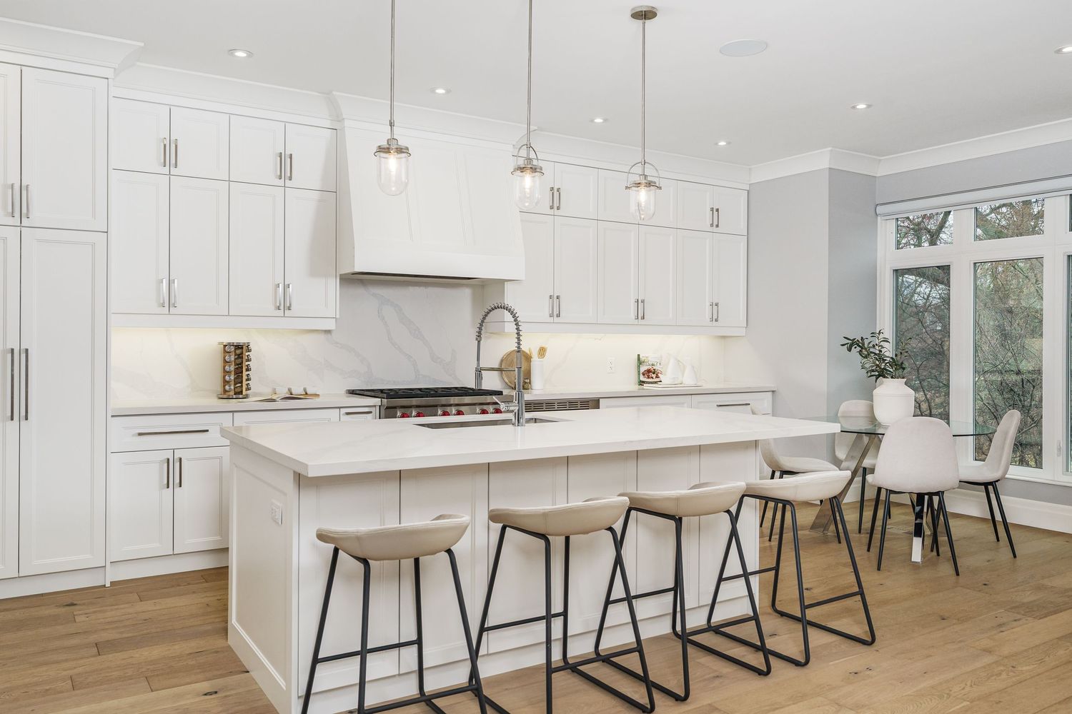 Modern white kitchen with hardwood floors features quartz countertops, pendant lights, and industrial bar stools at island.