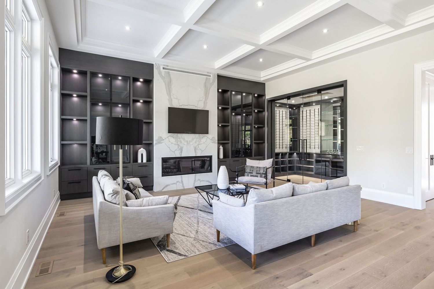 Elegant living room with built-in black shelving, white coffered ceiling, and modern gray sectional sofa.