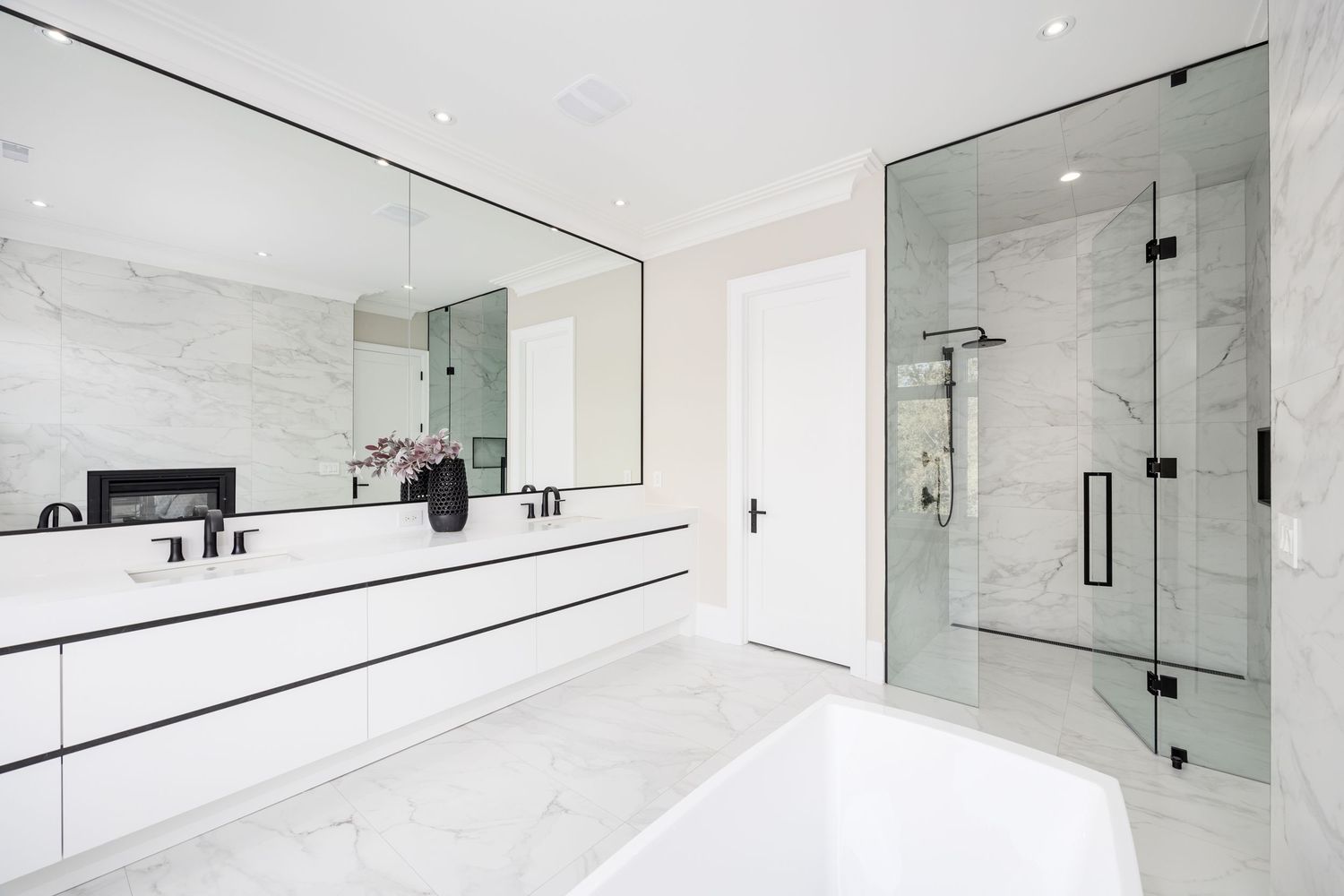 Minimalist white bathroom with glass shower enclosure and black hardware accents.