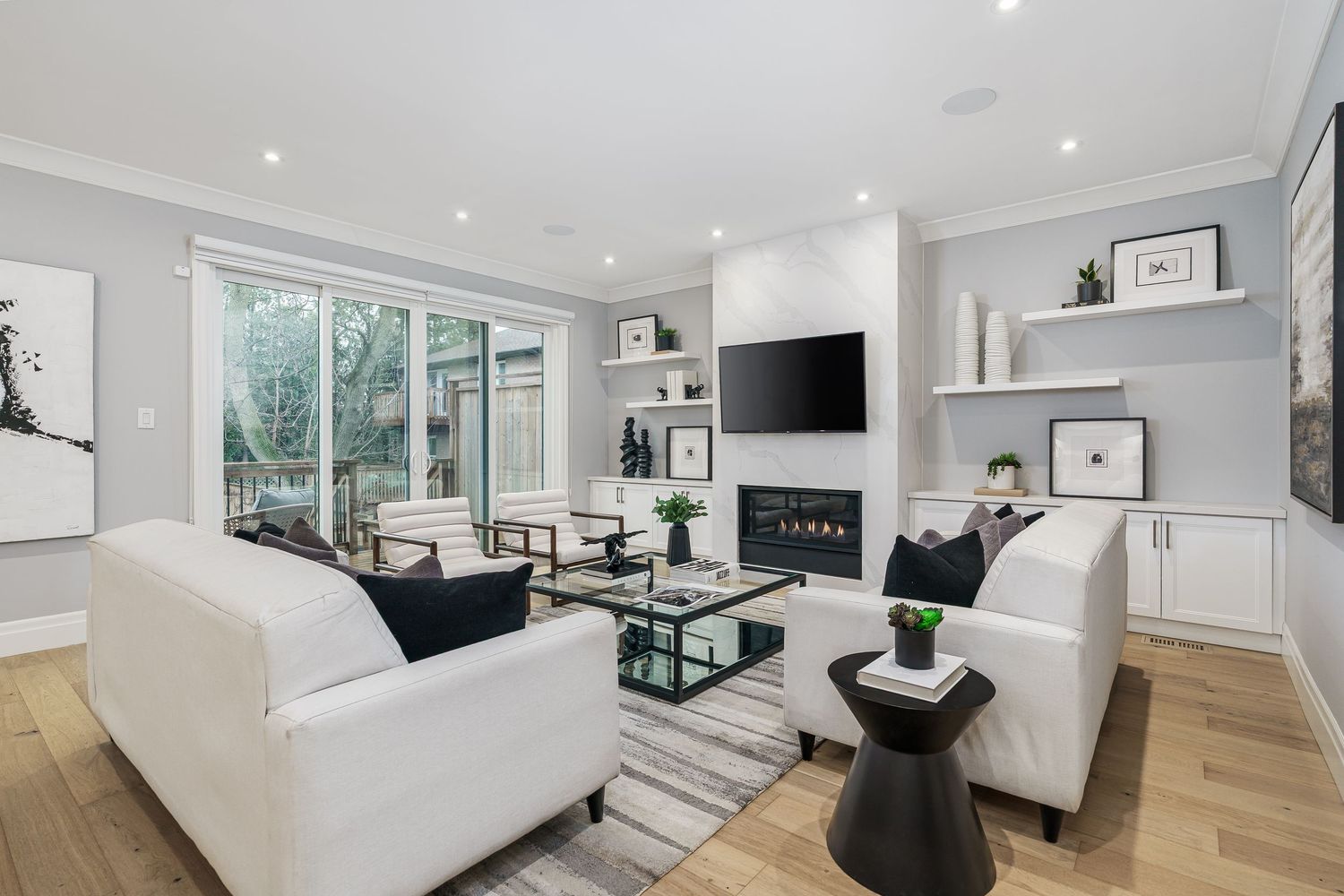 Modern bright living room with white sofas, built-in fireplace and floor-to-ceiling windows showcasing garden views.