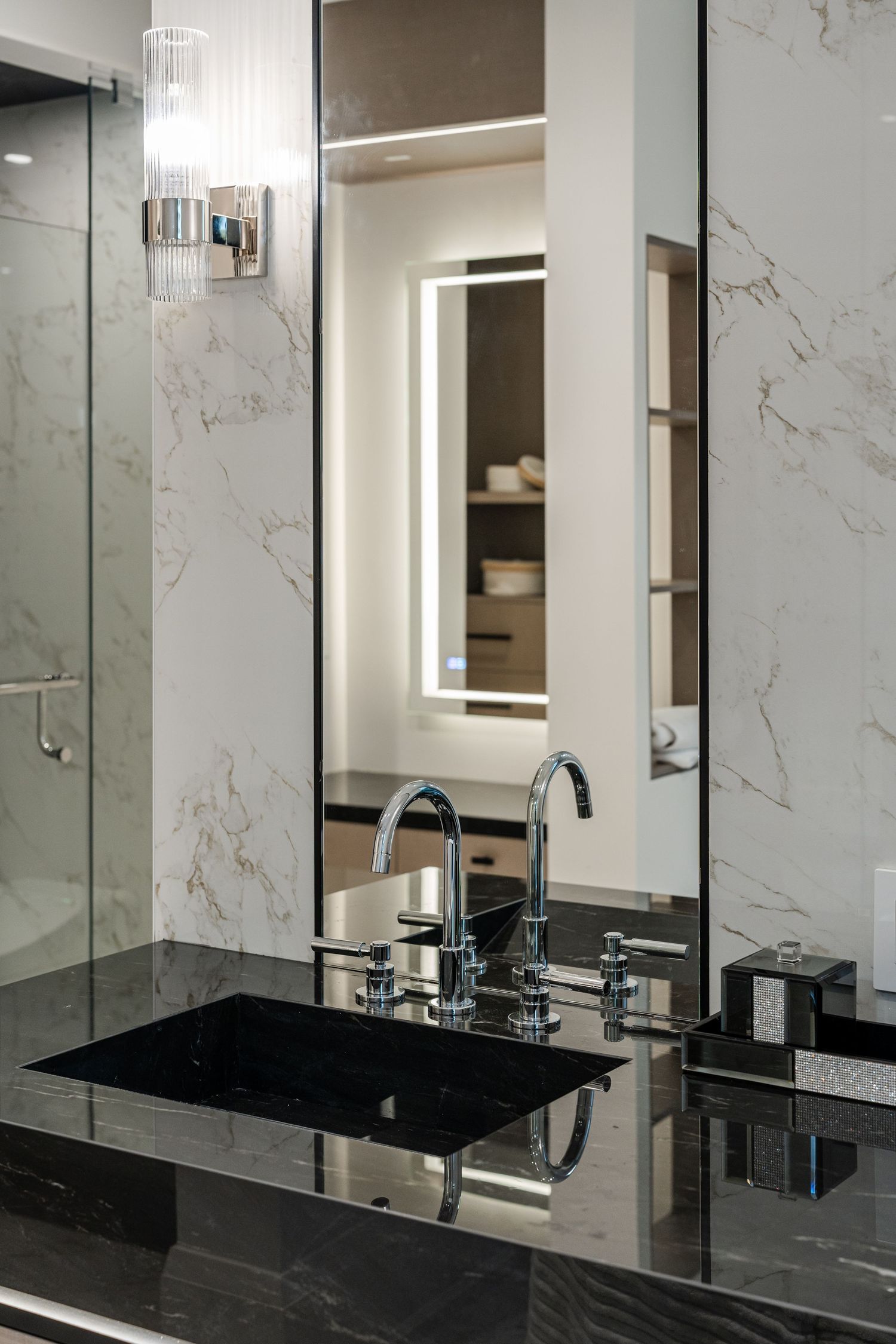Contemporary bathroom featuring black sink, chrome faucet, and illuminated mirror against marble walls.