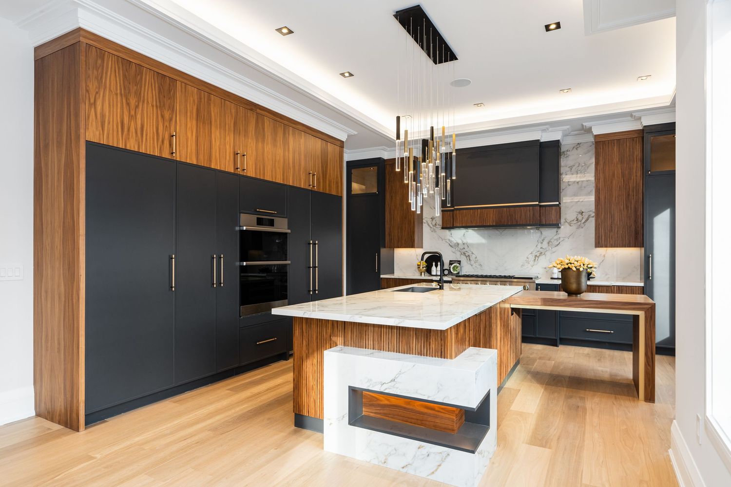 Modern kitchen with matte black cabinets, warm wood accents, and white waterfall island featuring pendant lighting.