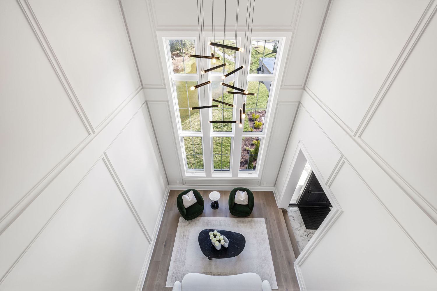 Elegant two-story living space with geometric chandelier and large windows overlooking garden.