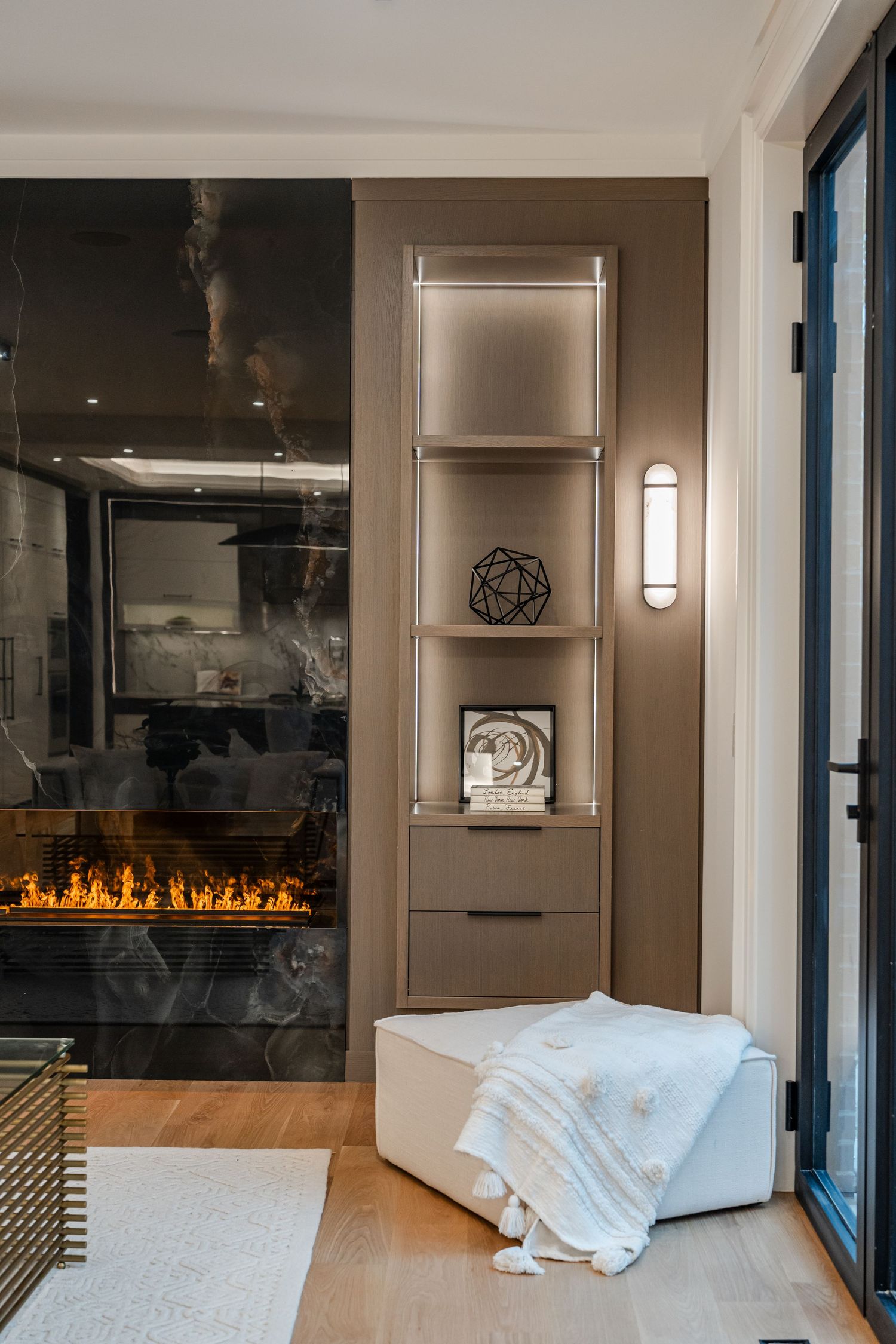 Contemporary living space with built-in shelving and linear gas fireplace with dark marble surround.