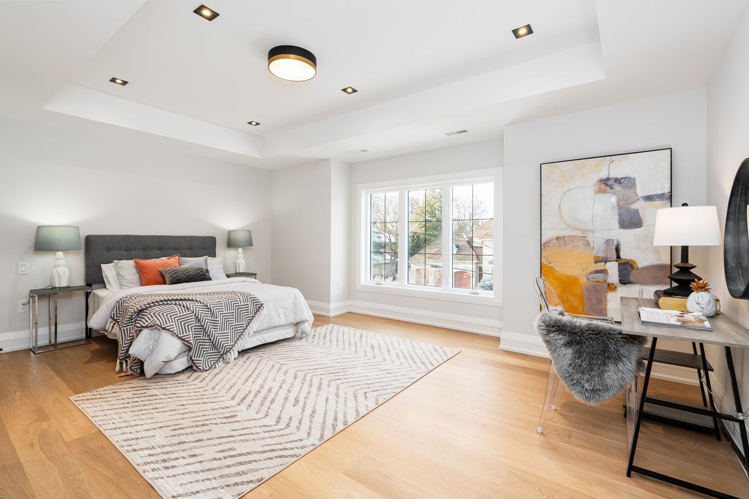 Bright bedroom with large windows, hardwood flooring, and geometric area rug.
