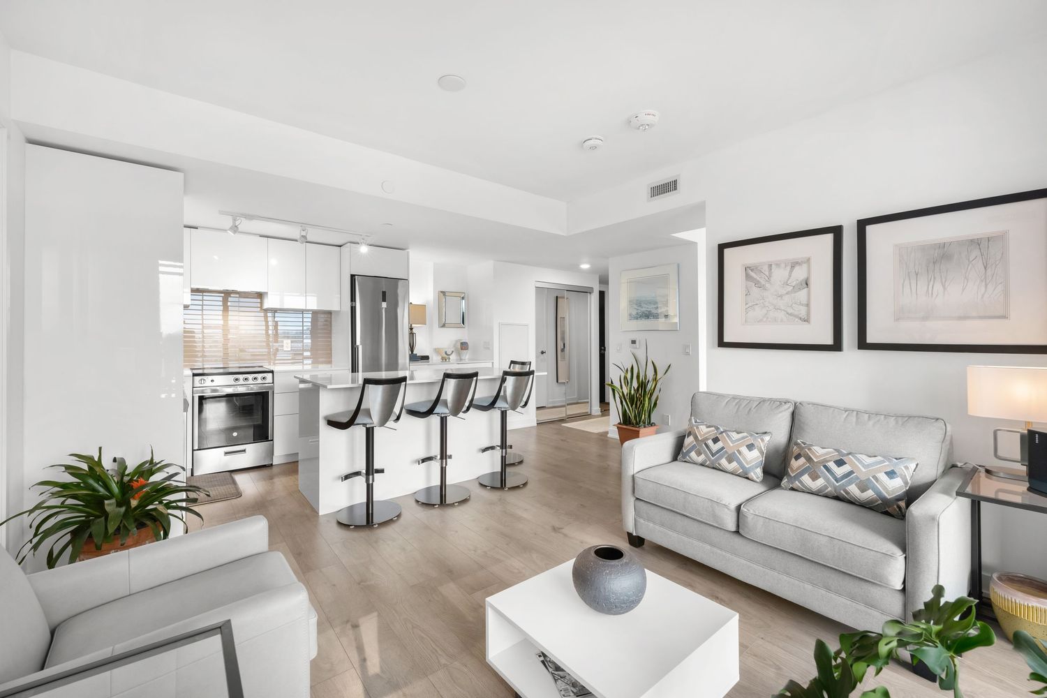 Modern open concept apartment interior with white furniture, breakfast bar, and hardwood floors in contemporary style.