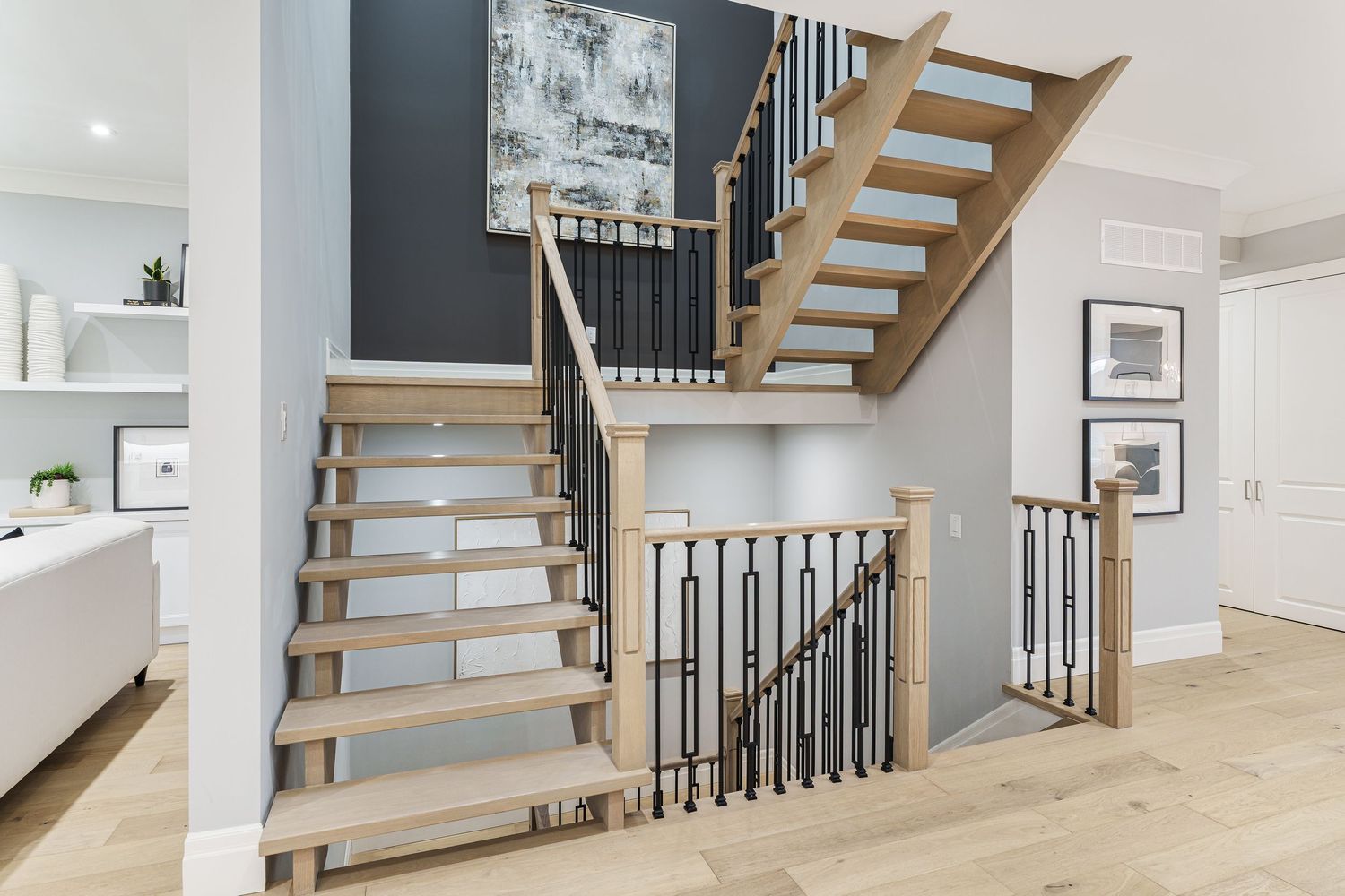 Modern wooden staircase with black metal railings and light hardwood floors in contemporary home interior.