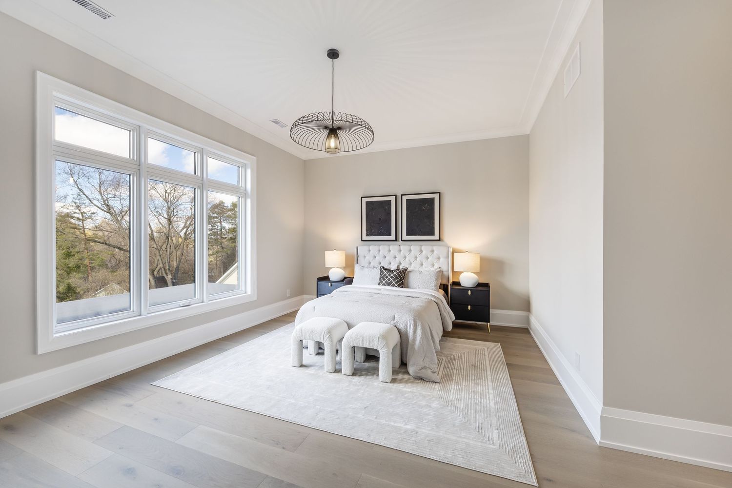 Minimalist bedroom design with geometric light fixture, white area rug, and large windows framing outdoor views.