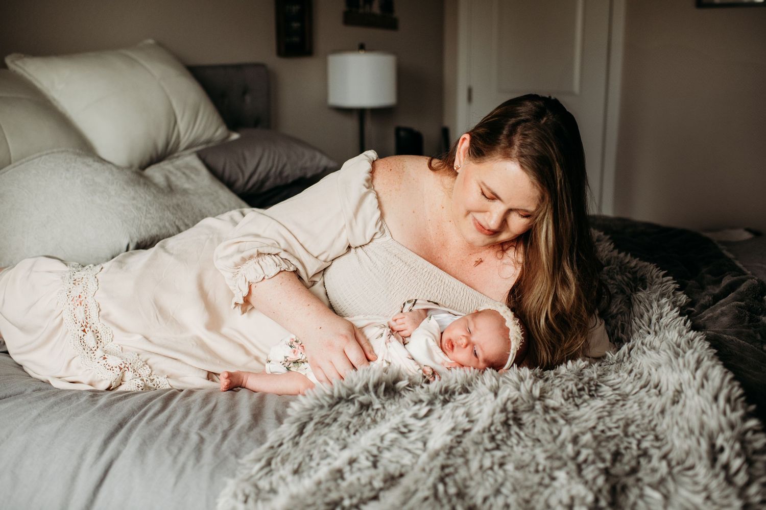 Two people share a tender moment lying together on a cozy bed with gray textured bedding and soft lighting.
