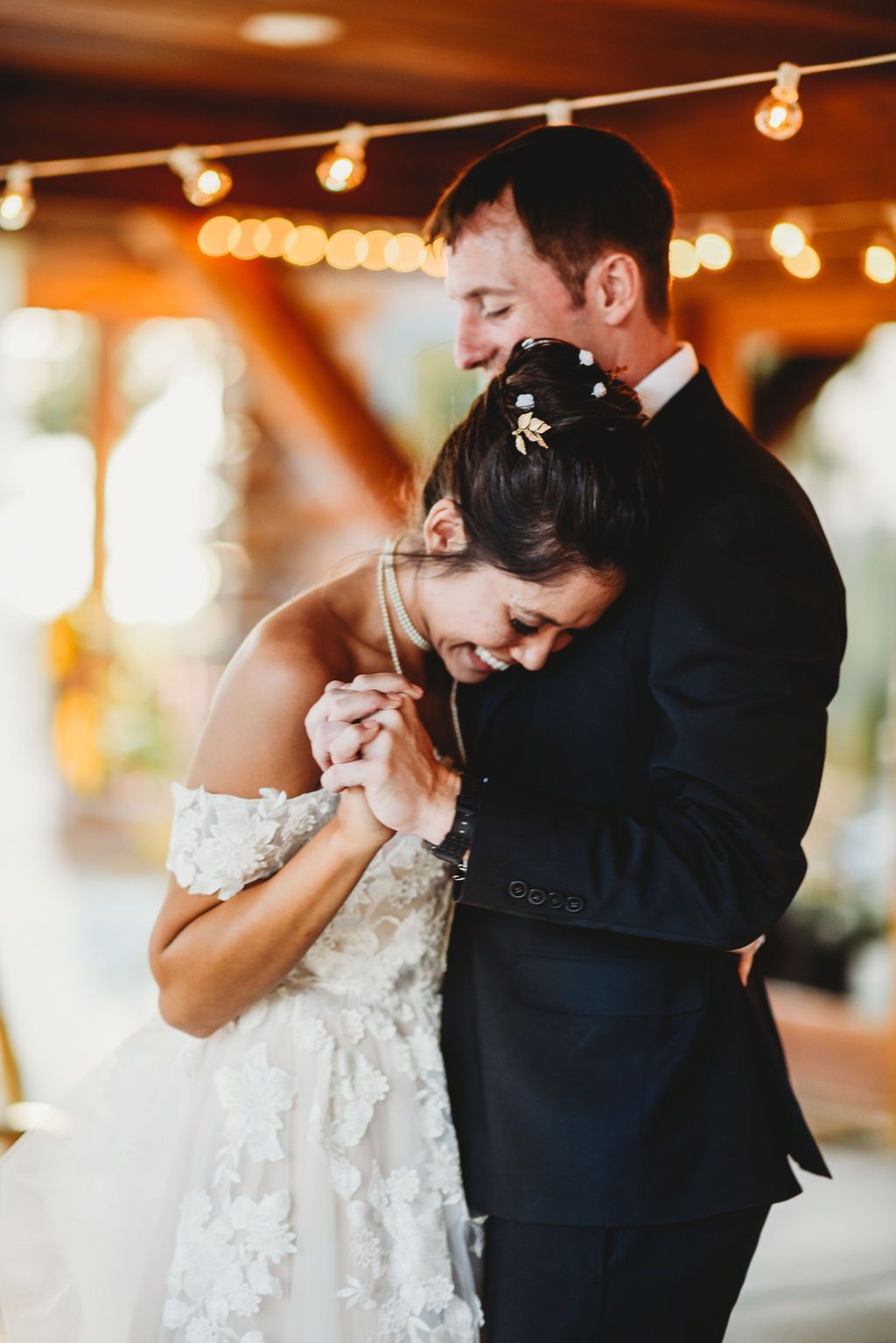 A tender moment between newlyweds dancing under warm string lights during their first dance.