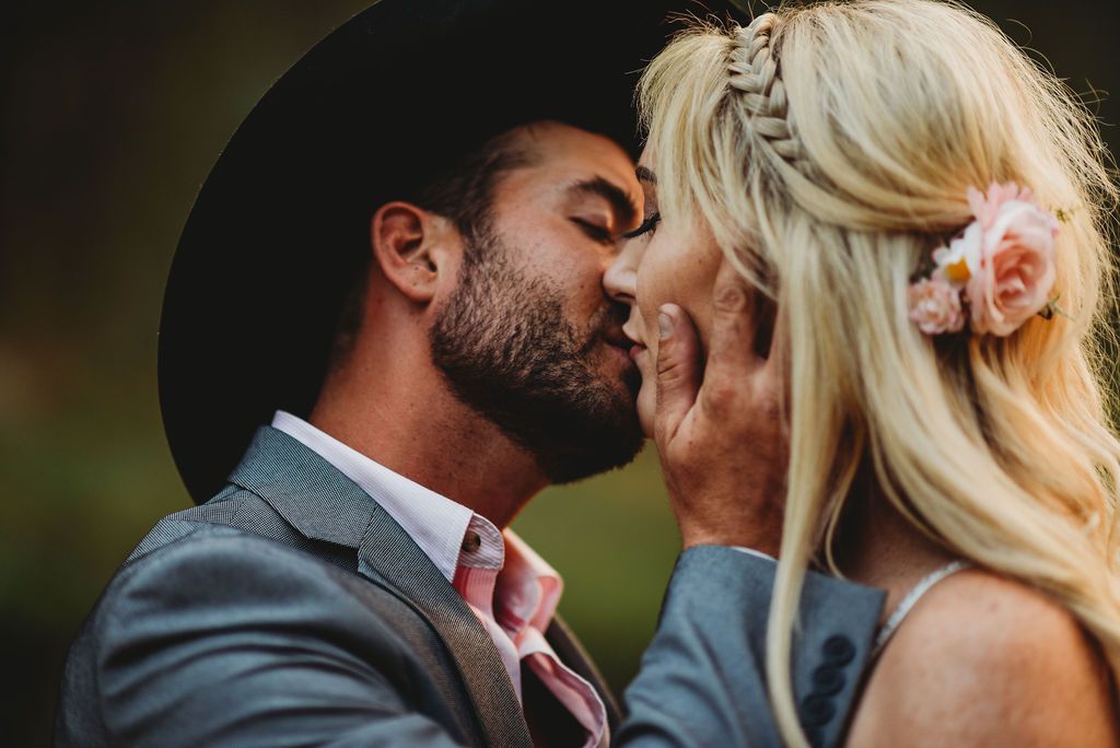 Intimate moment between newlyweds with one wearing a black hat and gray suit.
