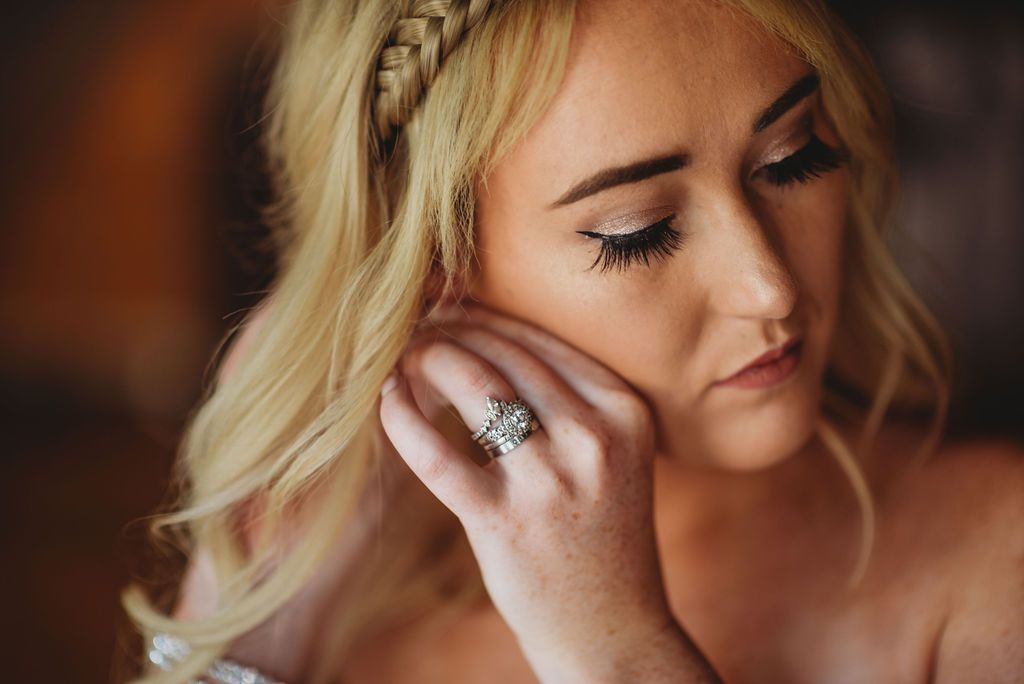 Close up shot of a diamond ring on hand with soft focus makeup and braided blonde hair details.
