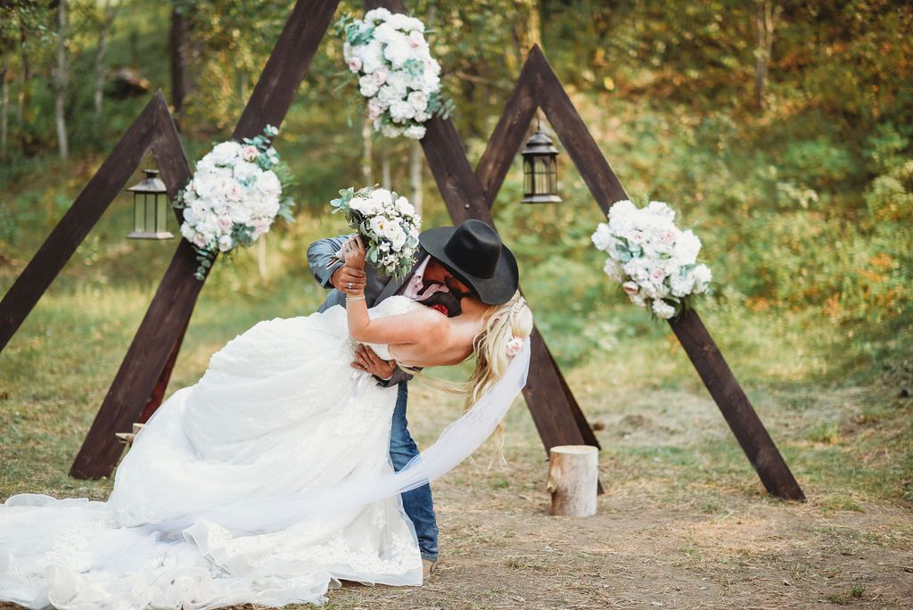 A romantic outdoor wedding scene with floral decorations and a rustic wooden triangle arch frame.