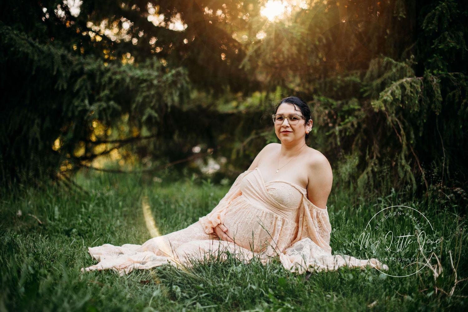 Maternity portrait in pink dress amid sunlit garden setting.