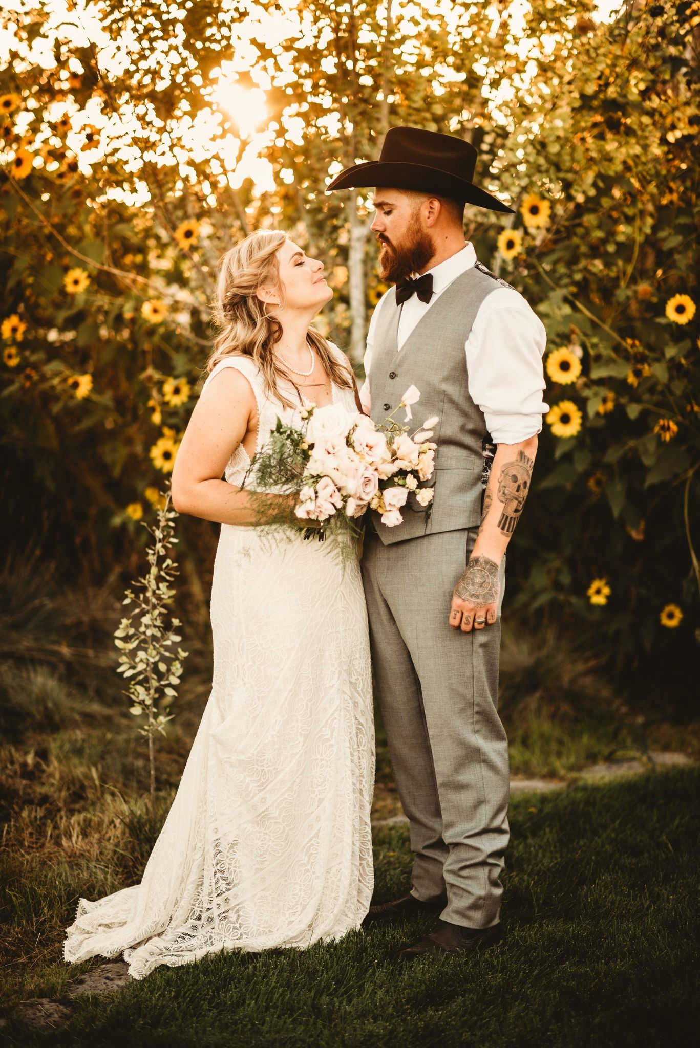 A beautiful wedding couple poses in front of sunflowers at sunset wearing rustic country attire.