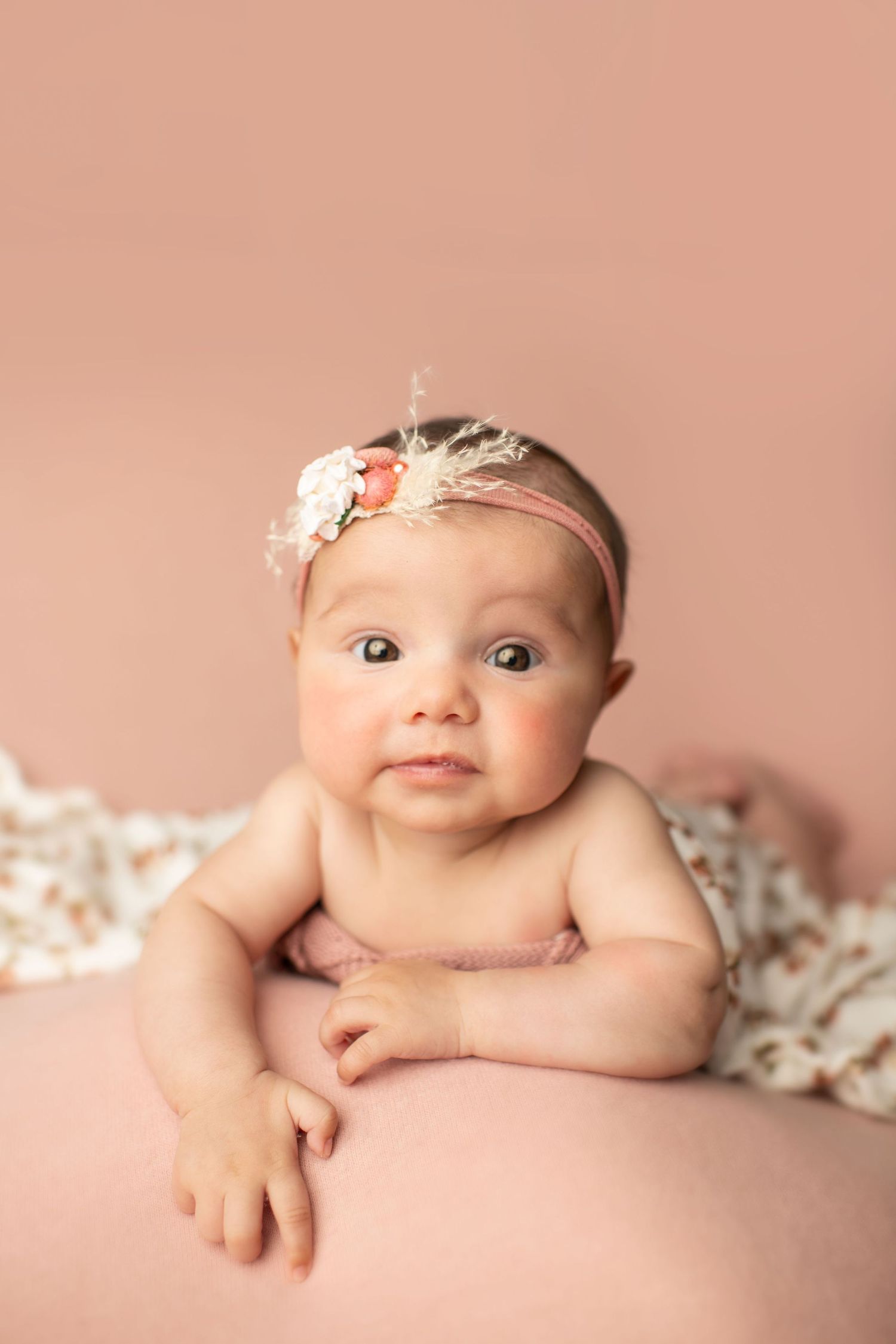 Baby in delicate floral headband posed on pink backdrop with lace detail.