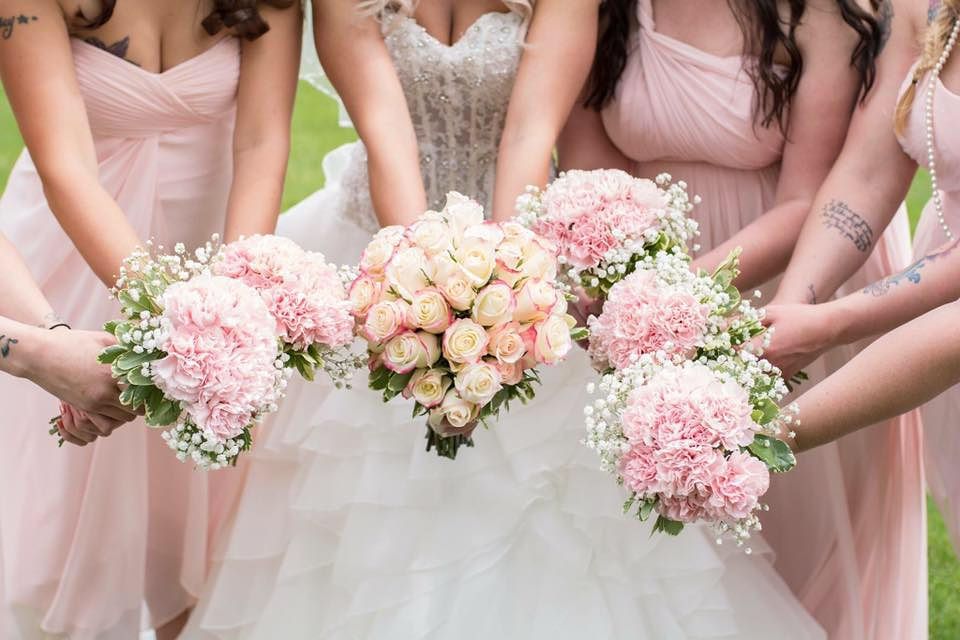 Pink bridesmaid bouquets and white dress are held together in a wedding party lineup showing delicate floral arrangements.