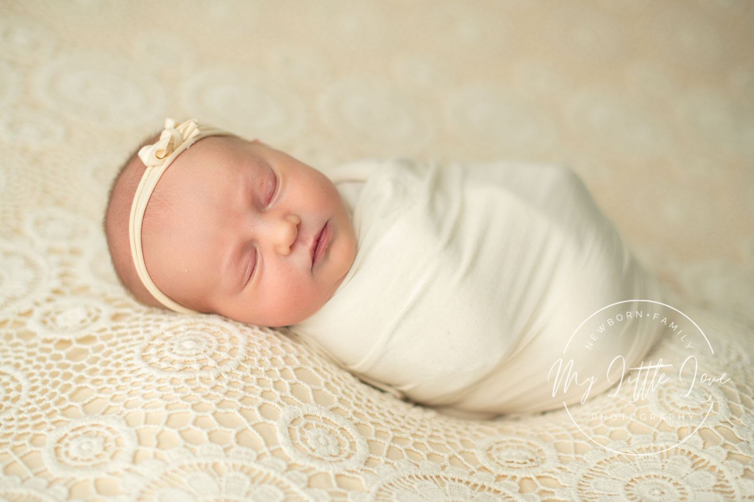 Peaceful sleeping newborn wrapped in soft white swaddle blanket resting on delicate lace fabric.