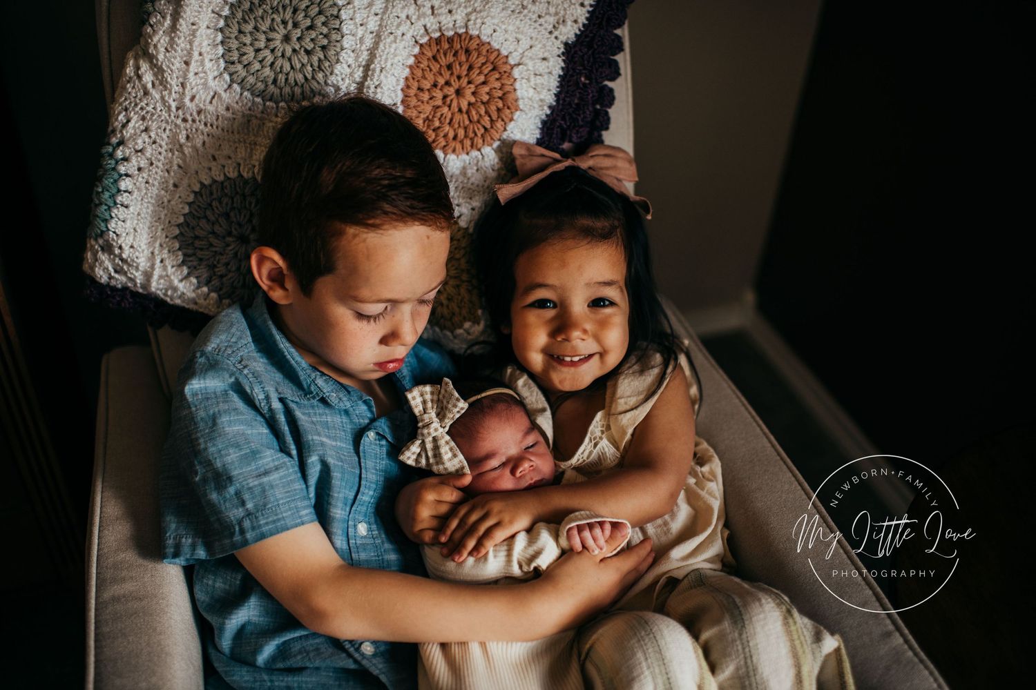Siblings carefully holding newborn baby against floral patterned backdrop.