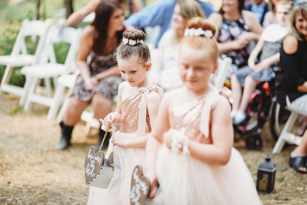 Two flower girls in pink dresses scatter petals during an outdoor wedding ceremony.