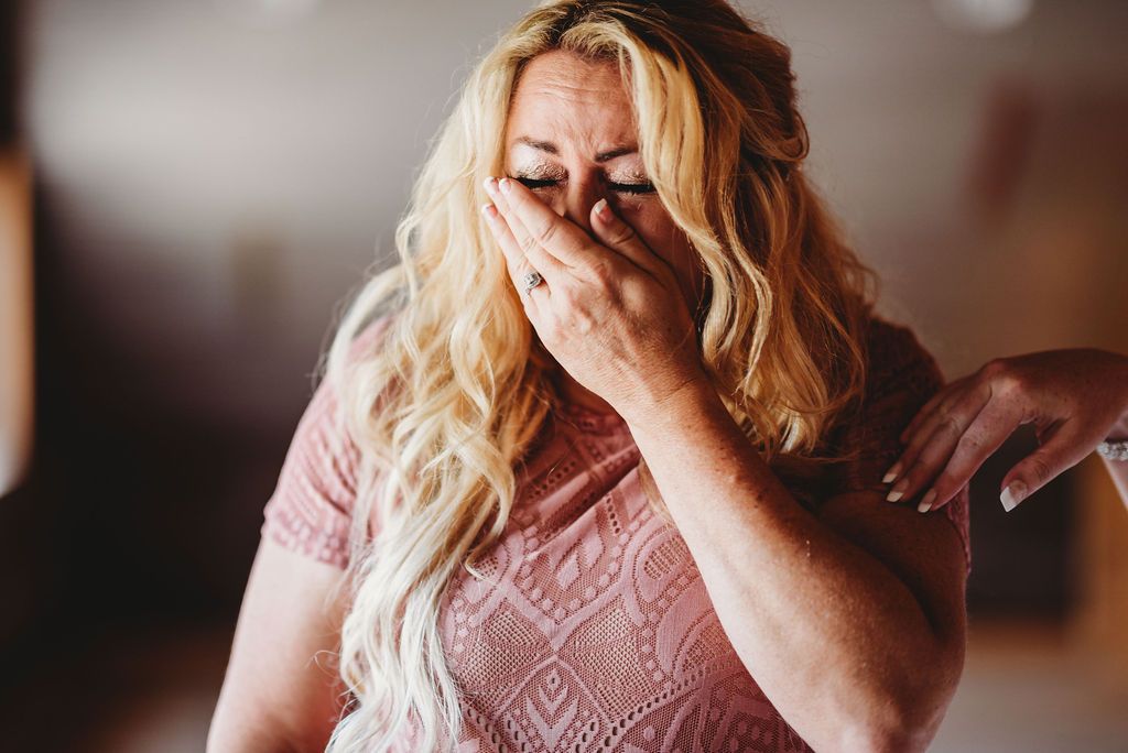 An emotional moment captured as someone in a pink lace dress wipes tears from their eyes.