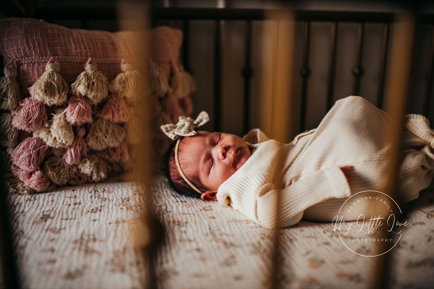Baby sleeping peacefully on textured bedding with pink decorative pillow in background.