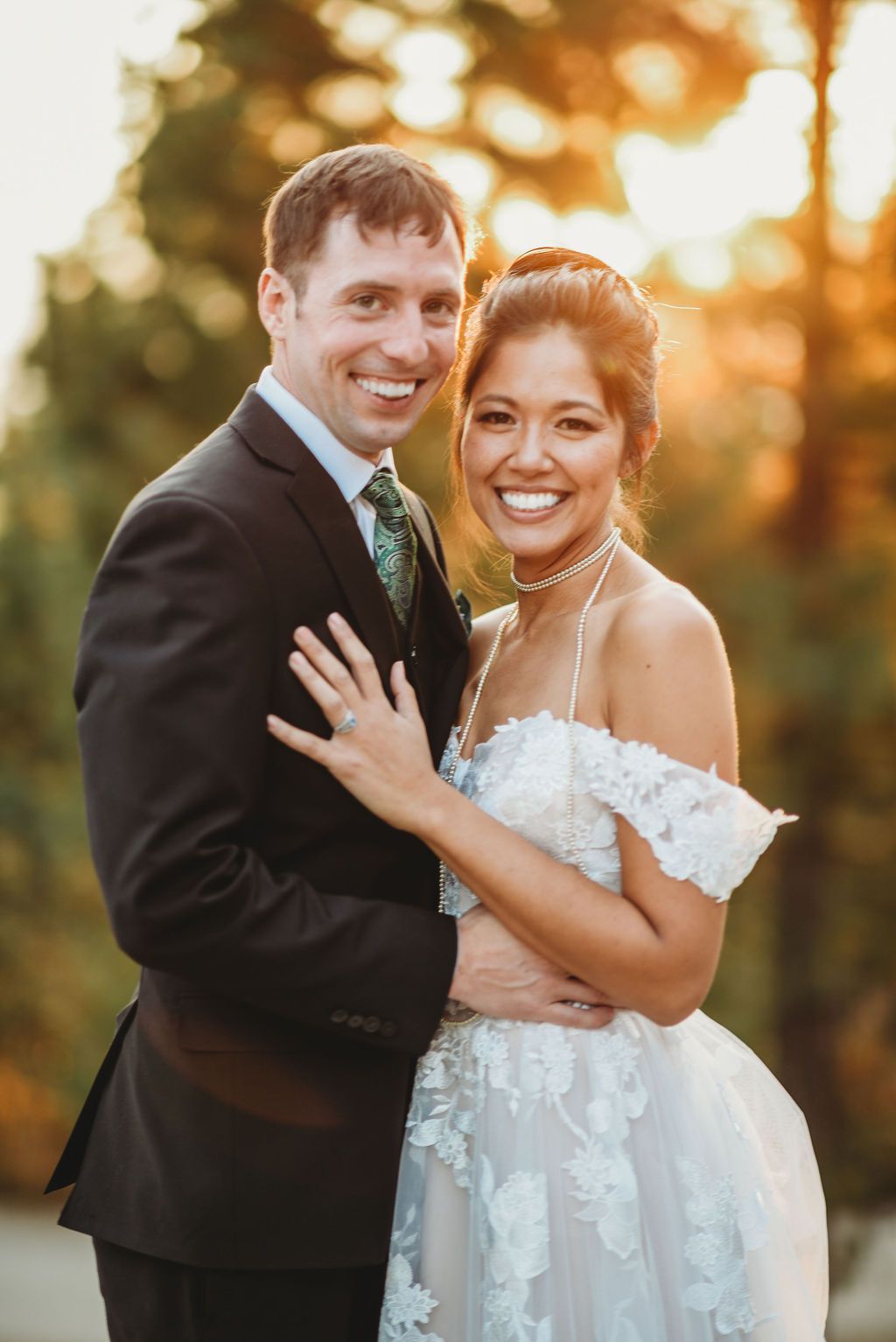 A happy newlywed couple embracing outdoors at sunset with golden bokeh lighting in the background.